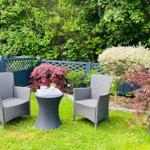 Garten mit zwei Stühlen und Tisch, umgeben von Pflanzen und Zaun.