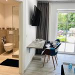Wohnbereich mit TV, Schreibtisch und Blick auf Garten. Nebenraum mit Dusche und Toilette.