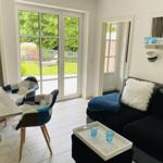 Wohnzimmer mit Sofa, Tisch und Stühlen. Durchgang zur Terrasse mit Gartenblick.