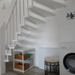 Washing machine next to white staircase and shelf with crates.