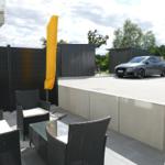 Terrace with seating group and yellow umbrella. Backyard with carport and car.
