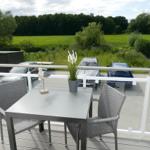 Terrace with table and chairs, view of green field and trees.