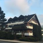 Mehrfamilienhaus mit Balkonen und Dachgauben. Vorgarten mit Holztor und Hecken.