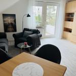 Wohnzimmer mit Sofa, Sessel, Tisch und Balkonzugang.
