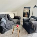 Wohnzimmer mit grauem Sofa, Sessel und Glas-Tisch. Wandbild und Stehlampe sind sichtbar.