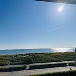 Meeransicht mit Sonne, Strandpromenade und Grünflächen.