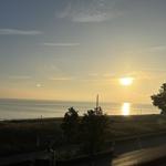 Sonnenuntergang über dem Meer mit Bäumen und Parkplatz im Vordergrund.