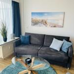Ein Wohnzimmer mit grauem Sofa, Glas-Tisch und Strandbild an der Wand.