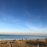 Strand mit Dünen, klarem Himmel und wenigen Menschen.