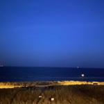 Nachtansicht vom Strand mit beleuchteten Weg und Meer im Hintergrund.