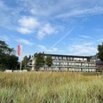 Modernes Mehrfamilienhaus mit Balkonen und Flagge vor Grasland.