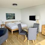 Schlafzimmer mit Bett, Esstisch und Fernseher. Holzboden und Wandbilder.