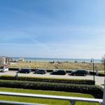 Blick auf Strand mit Parkplatz und Grünflächen unter blauem Himmel.