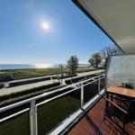 Terrasse mit Tisch und Stühlen, Blick auf Meer und Strandpromenade.