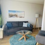 Wohnzimmer mit Sofa, Sessel, Glas-Tisch und Wandbild.