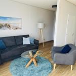 Wohnzimmer mit Sofa, Sessel und Glas-Tisch auf blauem Teppich