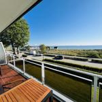 Terrasse mit Tisch und Stühlen, Blick auf Straße, Grünfläche und Meer.