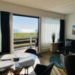 Wohn- und Essbereich mit Meerblick über Balkon. Schwarze Sofas, runder Tisch.