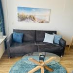 Ein Wohnzimmer mit grauem Sofa, Glas-Tisch und Wandbild.