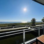 Balkon mit Blick auf Meer und Straße unter blauem Himmel.