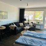 Wohnraum mit Schlafbereich, Sofa, Sessel und Balkon mit Blick auf Grünfläche.