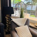 Ein grauer Sessel mit Kissen und Decke vor großem Fenster mit Blick auf Balkon.