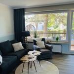 Wohnzimmer mit Sofa, Sessel und Blick auf Balkon mit Pflanzen.