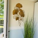 Wanddekoration mit goldfarbenen Blättern und Pflanze in einem Raum mit zweifarbigem Wandverputz.