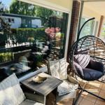 Terrasse mit Hängesessel, Sitzgruppe und Tisch. Blick auf grüne Umgebung.