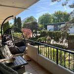 Terrasse mit Hängesessel, Tisch und Stühlen. Blick auf grünen Garten und Häuser.