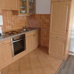 Küche mit Holzschränken, Herd und Spüle. Bodenfliesen und Stuhl sichtbar.