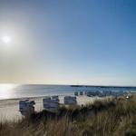 Strand mit Strandkörben und Steg unter blauem Himmel