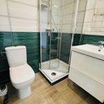 Badezimmer mit Dusche, Waschbecken und Toilette. Fliesenwand in Grün-Weiß.