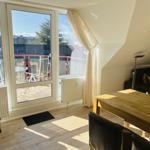 Wohnung mit Balkon, Essbereich und Schlafzimmer. Holzdielen und große Fenster.