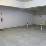 Untergeschoss-Parkplatz mit roter Tür und Feuerlöscher an der Wand.