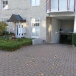Haus mit Eingang, Garage und gepflasterter Hof mit Hecken und Blumen.