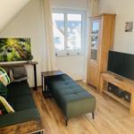 Wohnzimmer mit Sofa, Fernseher und Holzmöbeln. Fenster mit Blick auf Gebäude.