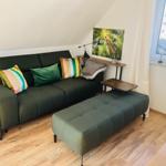 Ein Wohnzimmer mit grünem Sofa, Kissen und Holzboden. An der Wand hängt ein Bild.