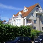 Mehrfamilienhaus mit Balkonen und rotem Dach unter blauem Himmel.
