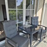 Terrasse mit zwei Stühlen und Tisch, daneben Glasfront und Garten.