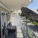 Terrasse mit Sitzgruppe, Sonnenschirm und Blick auf Straße mit Bäumen.