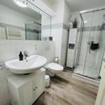 Badezimmer mit Dusche, Waschbecken und Toilette. Fliesenwand und Holzboden.