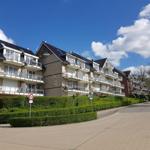 Reihenhaus mit Balkonen und begrünter Umgebung unter blauem Himmel.