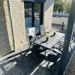 Terrace with table, chairs, and plants. Background: house wall and sliding door.