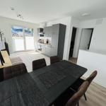 Dining area with table and chairs, kitchen, and terrace door in background.