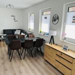 Living and dining area with sofa, table, chairs, windows with blinds, and wooden cabinet.