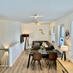 Living and dining area with sofa, table and chairs. Wooden floor and windows.