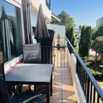 Terrasse mit Tisch, Stühlen und Sonnenschirm. Blick auf Garten und Straße.