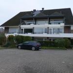 Zweistöckiges Haus mit Balkonen und gepflastertem Vorplatz. Ein Auto steht vor dem Haus.