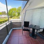 Terrasse mit Tisch und zwei Stühlen, Blick auf grüne Bäume und Rasenflächen.